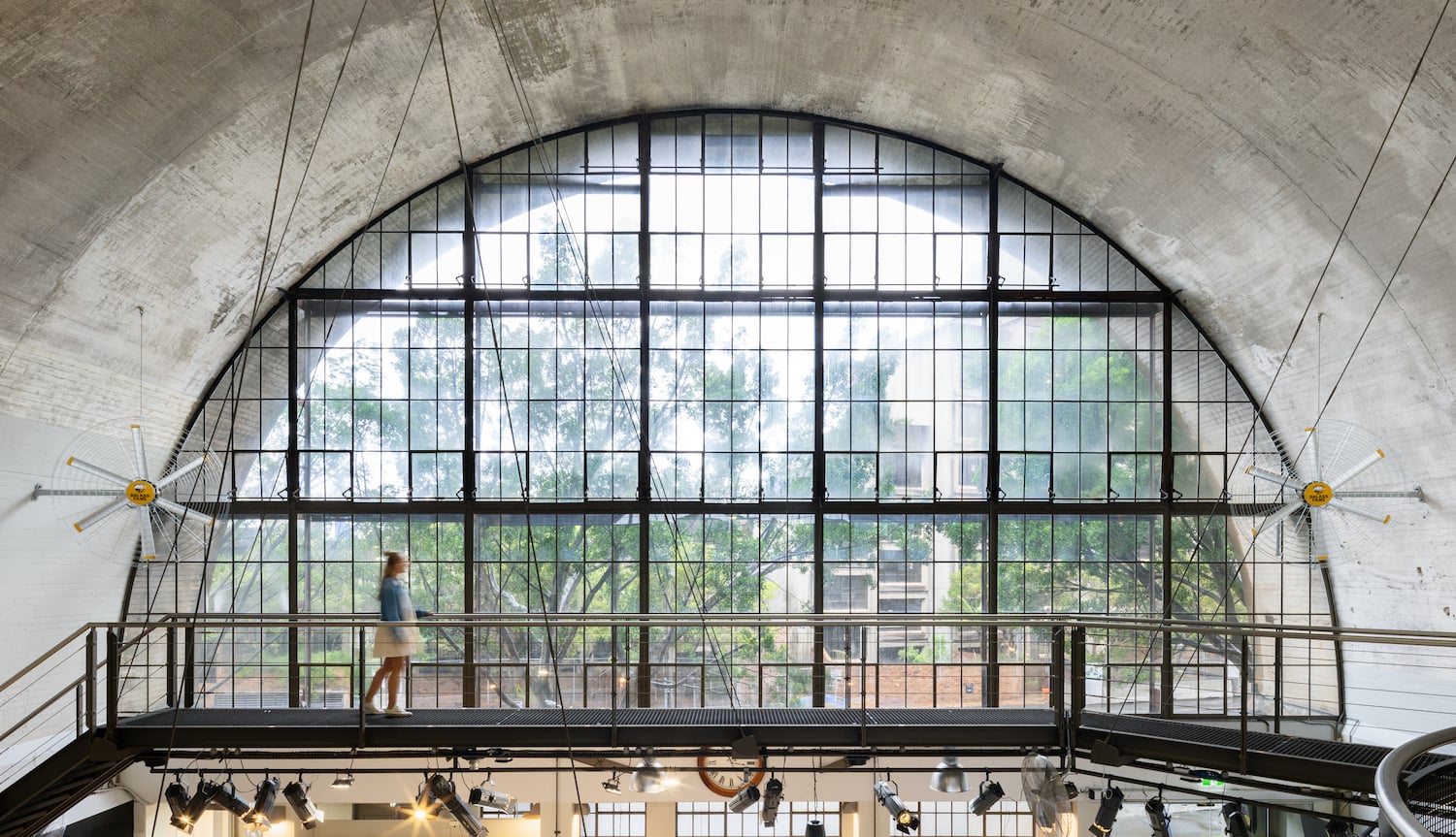 Wall-mounted directional fans installed in a large commercial space with arched ceiling and steel walkway