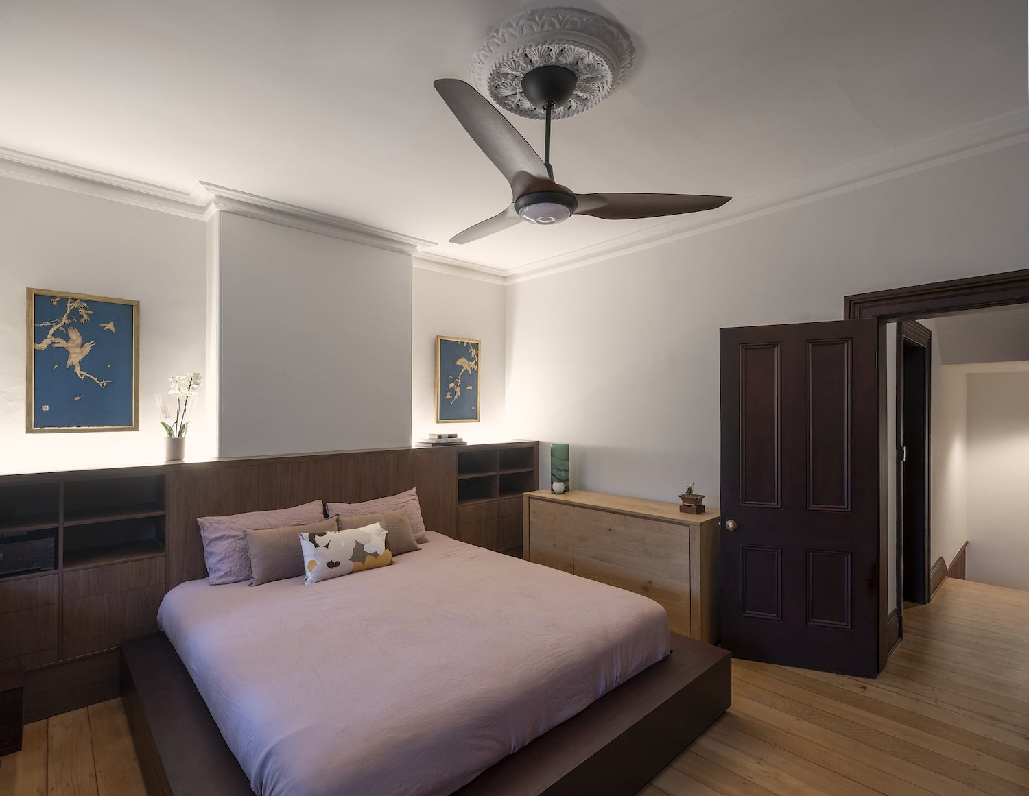 Ceiling fan with dark wood blades installed in a cozy residential bedroom with warm lighting